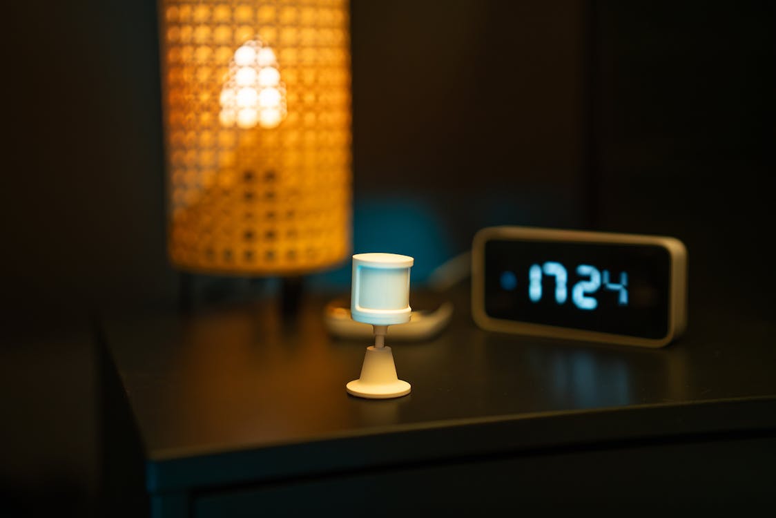 Een Zigbee temperatuursensor op een nachtkastje naast een slimme klok